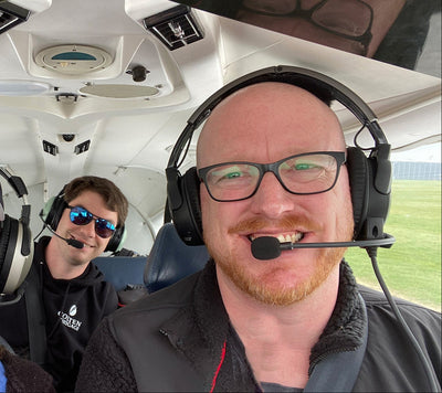 Two pilots inside an airplane cockpit, one smiling at the camera.